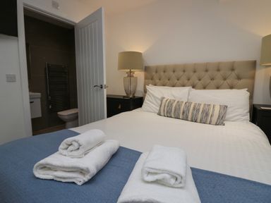 A bedroom with a bed with pillows and folded towels and a lamp on a bedside table at Edgemere Retreat in Cartmel