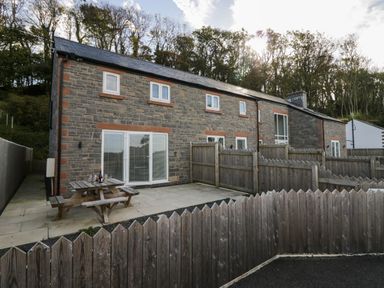 A stone house with multiple windows a patio table and wooden fences in the yard at Edgemere Retreat in Cartmel