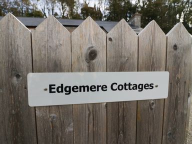 A wooden fence with a white sign reading Edgemere Cottages