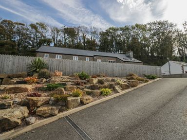 A driveway with a rock garden and wooden fence in front of a house with trees in the background at Edgemere Retreat in Cartmel