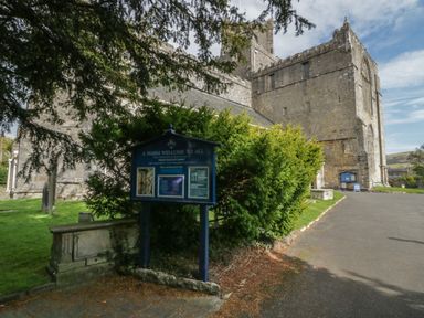 An exterior view of a stone church with a signboard and greenery at Edgemere Retreat in Cartmel