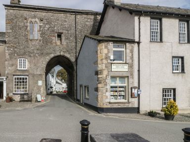 A street with an old stone archway and a bookshop building with windows at Edgemere Retreat in Cartmel