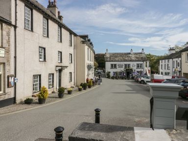 A street with parked cars and white buildings with signs including Kings Arms at Edgemere Retreat in Cartmel