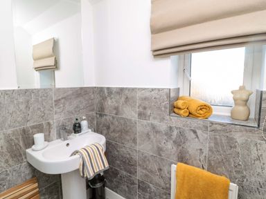 A bathroom with a pedestal sink with soap and towel a window with rolled towels and a mannequin bust at Coastal Retreat in Seahouses