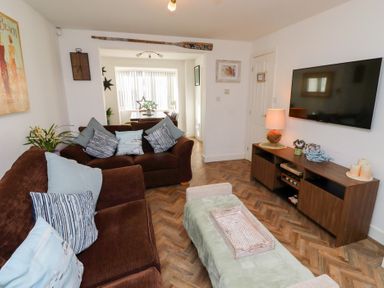 A living room with brown sofas cushions a green ottoman a wooden TV stand and a wall-mounted TV at Coastal Retreat in Seahouses