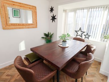 A dining area with a wooden table, four brown chairs, a plant on the table, a mirror on the wall, and two star decorations on the wall at Coastal Retreat in Seahouses