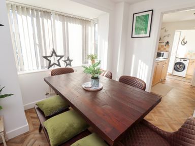 A dining area with a wooden table surrounded by brown chairs and a bench with green cushions at Coastal Retreat in Seahouses
