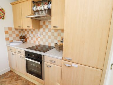 A kitchen with wooden cabinets an electric stove oven and a basket with bread at Coastal Retreat in Seahouses