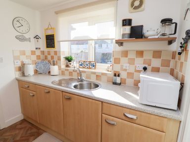 A kitchen countertop with a sink microwave kettle and shelves under a window at Coastal Retreat in Seahouses