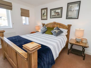A bedroom with a wooden bed striped bedding pillows and two bedside tables with lamps at Coastal Retreat in Seahouses