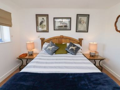 A bedroom with a wooden bed frame two side tables with lamps and bird artwork on the wall at Coastal Retreat in Seahouses