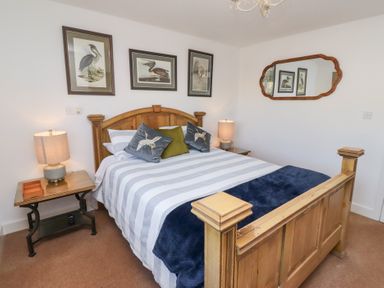 A bedroom with a wooden bed, two bedside tables with lamps, three bird paintings, and a mirror on the wall at Coastal Retreat in Seahouses