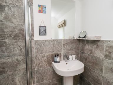 A bathroom with a pedestal sink a large mirror stone tiled walls and small wall decorations at Coastal Retreat in Seahouses