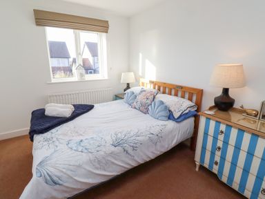 A bedroom with a wooden bed and blue striped dresser near a window at Coastal Retreat in Seahouses