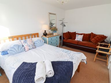 A bedroom with a bed a striped chest of drawers a lamp a mirror a sofa and a chair at Coastal Retreat in Seahouses