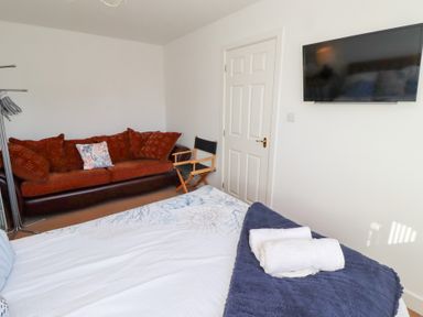 A bedroom with a bed a brown sofa a director chair a wall-mounted television and folded towels on the bed at Coastal Retreat in Seahouses