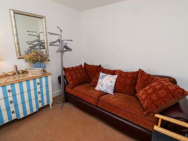 A room with a brown sofa with red cushions a striped blue and white dresser a mirror and a clothes rack at Coastal Retreat in Seahouses