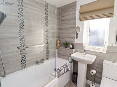 A bathroom with a bathtub shower combination a pedestal sink a toilet and a window with a blind at Coastal Retreat in Seahouses