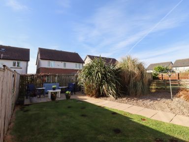 A backyard garden with grass, patio furniture, plants, and a clothesline at Coastal Retreat in Seahouses