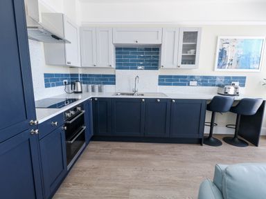 A kitchen with appliances and bar stools at Apartment 1 in Weymouth