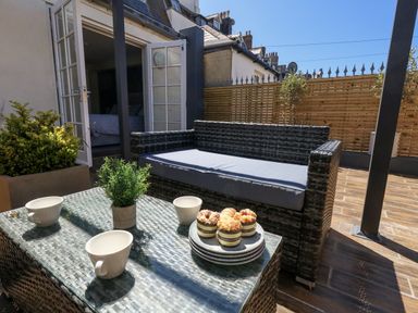 An outdoor seating area with a sofa, table, cups, and muffins at Apartment 1 in Weymouth