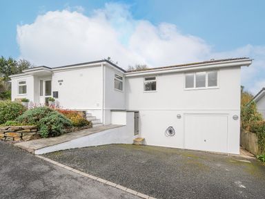 A white single-story house with a driveway shrubs and a garage at Seamay in Polzeath