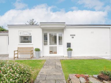 Front entrance of white single story house with glass door bench and garden at Seamay Polzeath