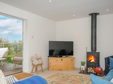 A living room with a wood stove television wooden chest and chair with blankets at Seamay in Polzeath