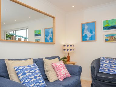 A living room with blue sofas patterned cushions a wooden side table with a lamp and framed artwork on the wall at Seamay in Polzeath