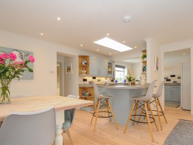A kitchen and dining area with a wooden table and gray chairs and bar stools at Seamay in Polzeath