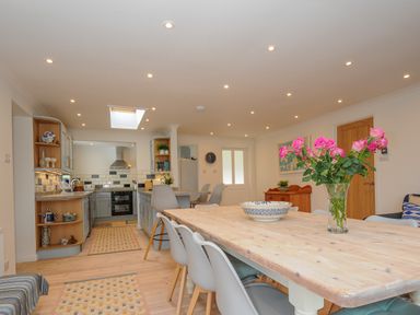 A kitchen and dining area with a wooden table and vase of pink flowers at Seamay Polzeath