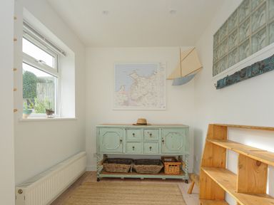 A small room with a window radiator a green cabinet with baskets underneath a wooden shelf a map on the wall and a model sailboat at Seamay Polzeath