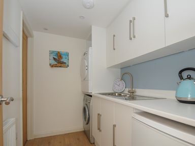 A utility room with a washing machine dryer sink clock and kettle at Seamay in Polzeath