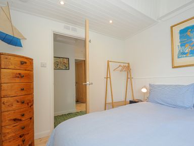 A bedroom with a wooden chest of drawers a wooden garment rack with hangers a bed with blue and white striped bedding and a framed artwork on the wall at Seamay in Polzeath