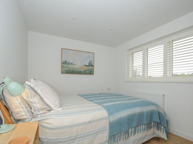 A bedroom with a bed covered with striped bedding and a blue blanket a lamp on a wooden nightstand and a painting on the wall at Seamay in Polzeath