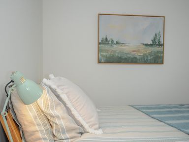 A bed with pillows and a lamp beside it with a landscape painting on the wall at Seamay in Polzeath