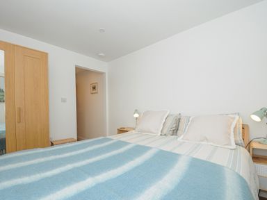 A bedroom with a double bed two bedside tables with lamps and a wooden wardrobe at Seamay in Polzeath