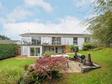 A garden with a patio area and outdoor furniture behind a two story white house with a balcony at Seamay in Polzeath