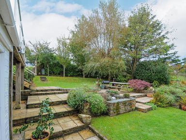 A garden with stone steps a patio table and trees at Seamay in Polzeath