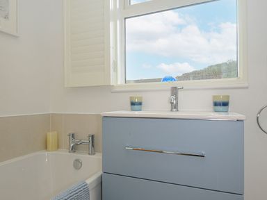 A bathroom with a bathtub a blue vanity unit and a window with a view at Seamay in Polzeath