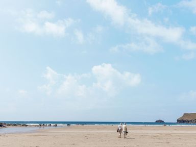 A sandy beach with people walking near the shoreline and calm ocean waves at Seamay in Polzeath