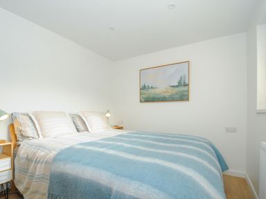 A bedroom with a bed covered by blue and white striped blankets and landscape painting on the wall at Seamay in Polzeath