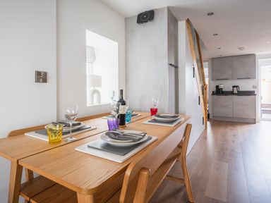 A dining table set with plates and glasses next to a kitchen with cabinets and appliances at Hoheck in Abersoch