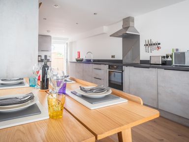 A kitchen with a wooden dining table set with plates glasses and a bottle of wine at Hoheck in Abersoch