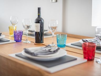A dining table with plates, cutlery, wine glasses, colorful drinking glasses, and a bottle of wine at Hoheck in Abersoch