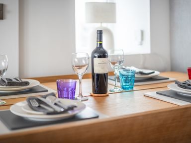 A dining table set with plates forks knives napkins wine glasses colored water glasses and a bottle of Mascota Malbec wine at Hoheck in Abersoch