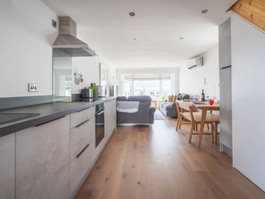 A kitchen and living room with gray sofas a wooden dining table and wooden flooring at Hoheck in Abersoch