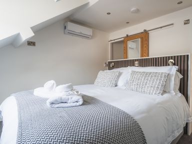 A bedroom with a bed made up with white linens and decorative pillows at Hoheck in Abersoch