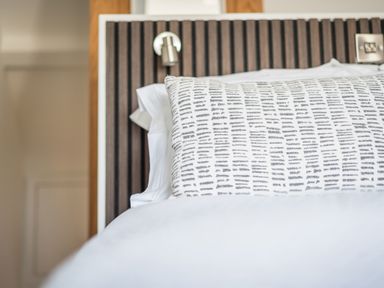 A close up of a bed with a patterned pillow and a wooden slatted headboard at Hoheck Abersoch