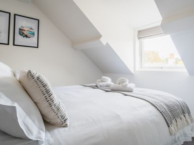A bedroom with a bed with white linens pillows folded towels and a window under a slanted ceiling at Hoheck in Abersoch